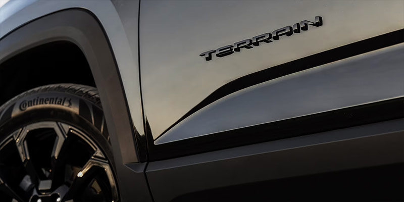 Close-up of a black 2025 GMC Terrain with the 'Terrain' logo and a Continental tire in the background.